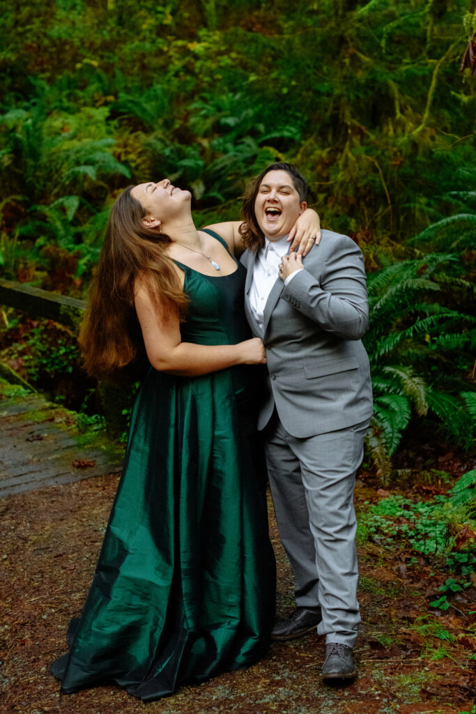 Two brides laughing on the bridge during forest engagement session