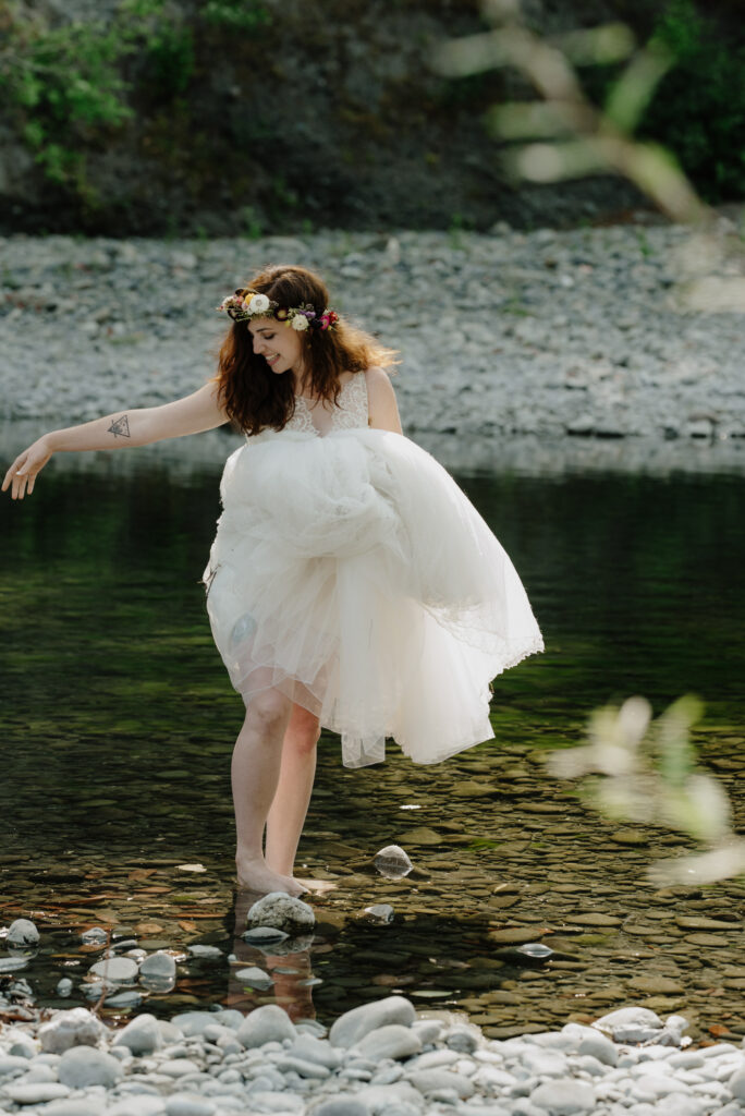 Bride reaches for groom's hand as they wade in the Van Duzen river