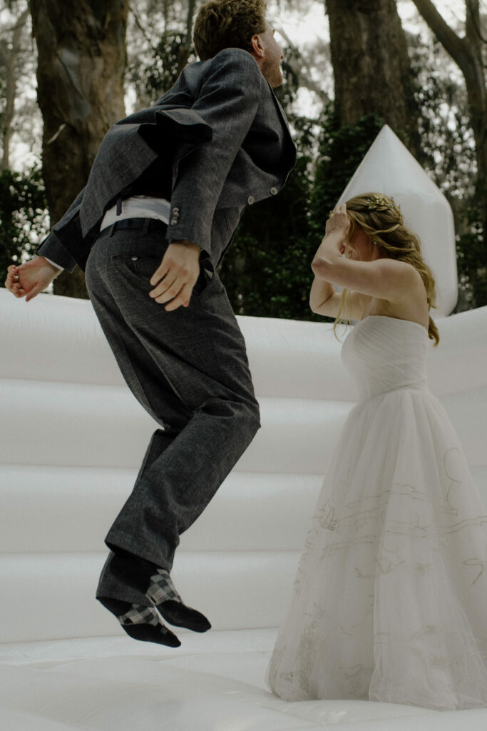 Bride and groom jump together in a white bouncy castle at the Oyster Beach cabins - Humboldt Bay Social Club