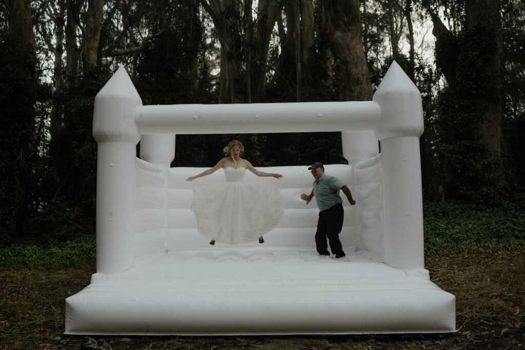 Bride and father bounce in white bouncy castle at Oyster Beach - Humboldt Bay Social Club in Northern California