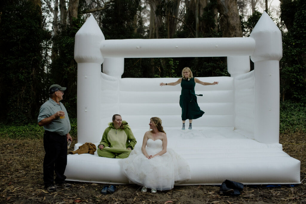 Mom jumps in the bounce house while guests chat at Humboldt Bay Social Club Oyster Beach wedding