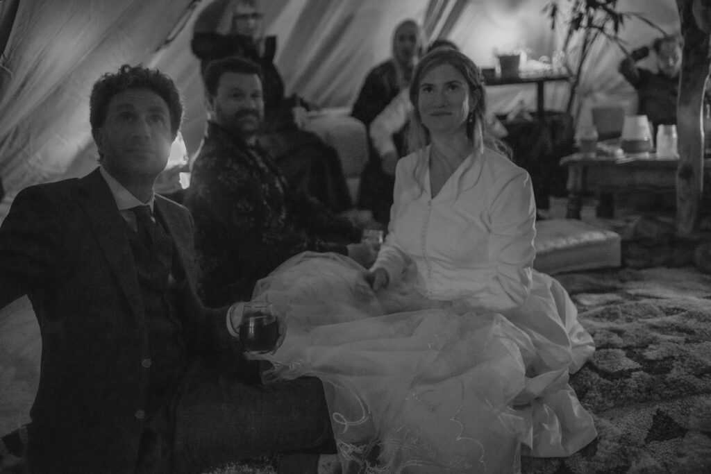 Wedding guests lounge with bride and groom in canvas bell tent at night at Humboldt Bay Social Club Oyster Beach in Northern California