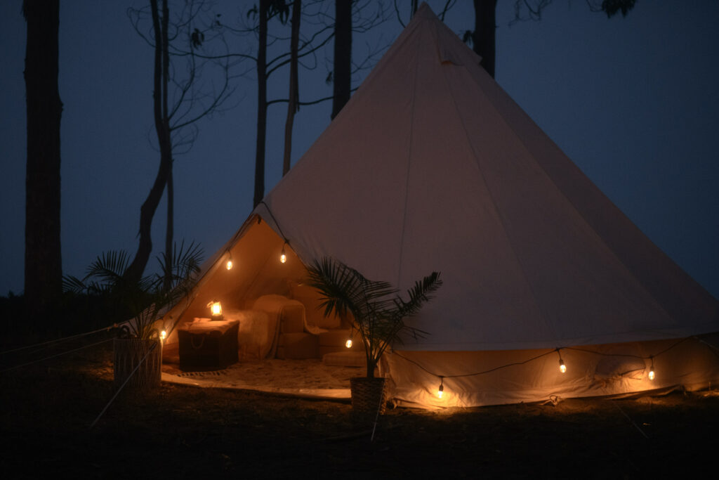 Canvas glamping tent at dusk lit by string lights with eucalyptus trees and Humboldt Bay in the distance