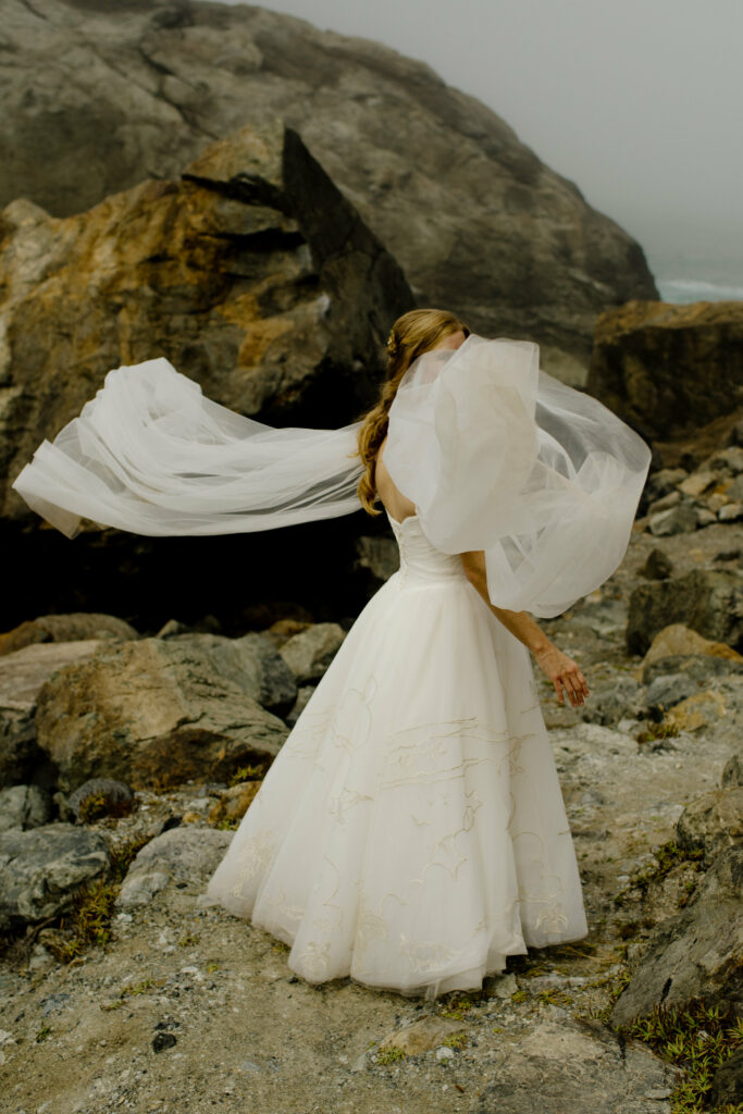 Bride floats her wedding cape in the wind on the Redwood coast in Northern California