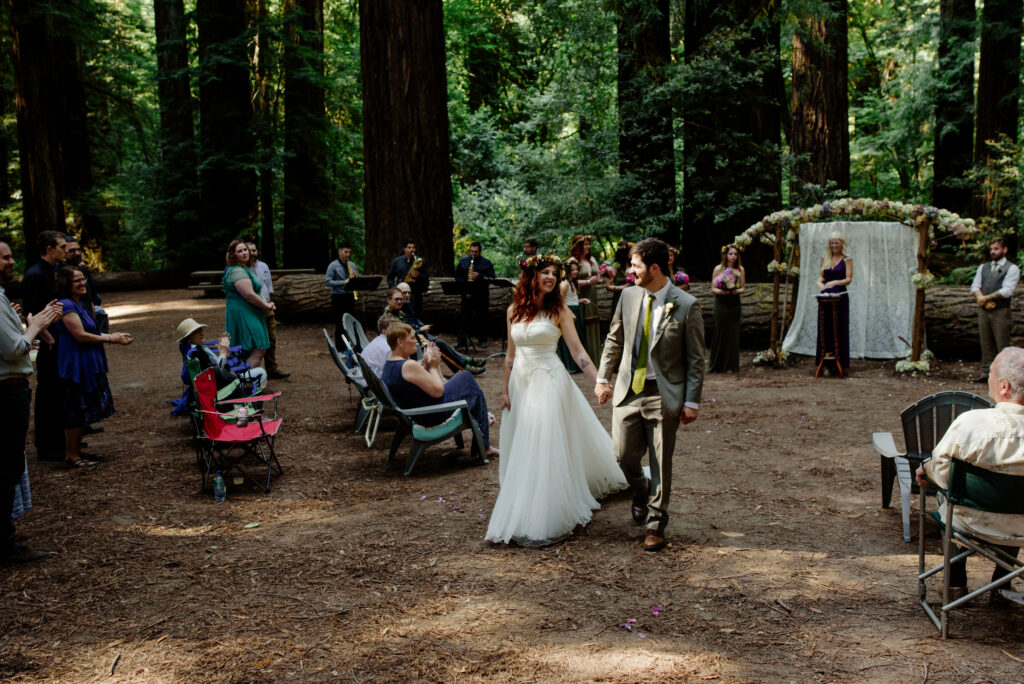 Newly married couple walks back down redwood aisle after ceremony in Pamplona Grove.