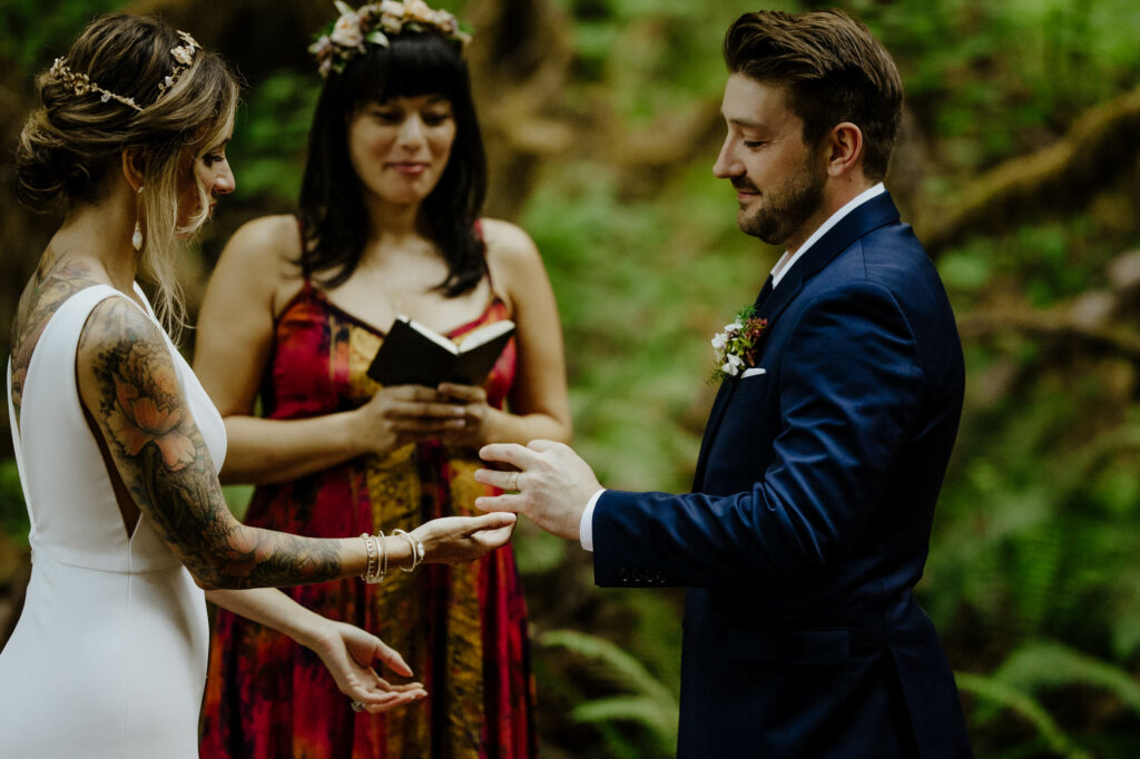 Bride pauses after putting ring on grooms finger during redwood national forest wedding ceremony