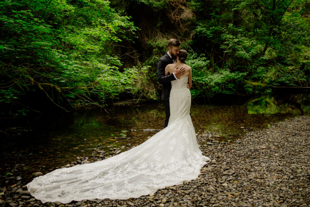 Bride with long lace train by a creek in Redwood National Park