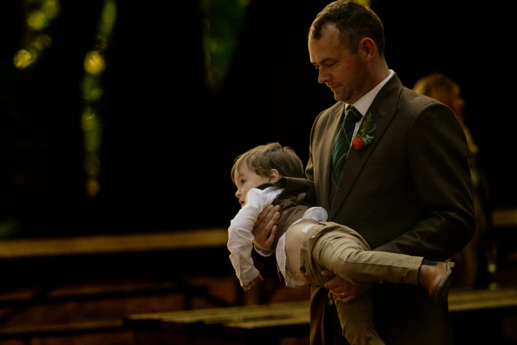Wedding guest carries toddler through redwood grove reception