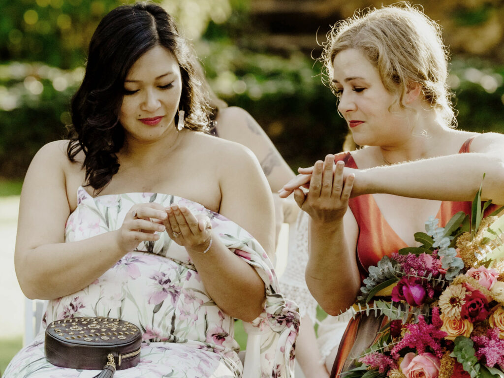 Two guests in colorful floral gowns bless rings at a late summer wedding ceremony for two brides in Northern California at the Benbow Inn