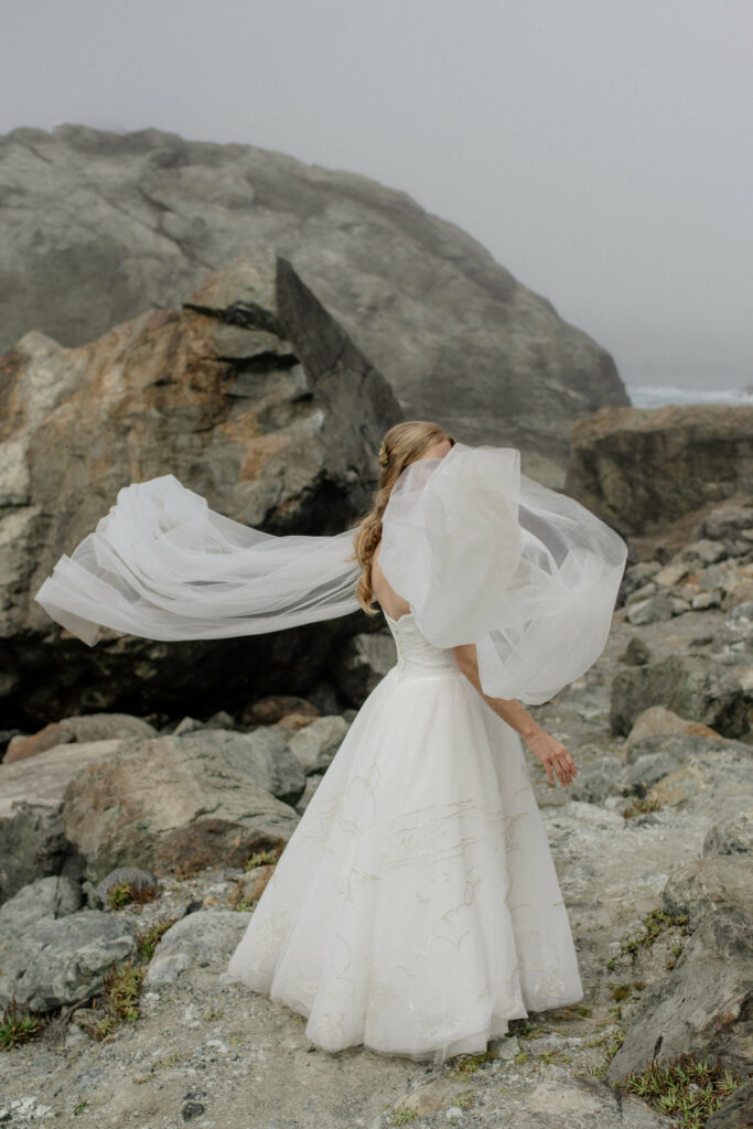 Sheer cape catches the coastal breeze during a bridal portrait session near Wedding Rock in Northern California