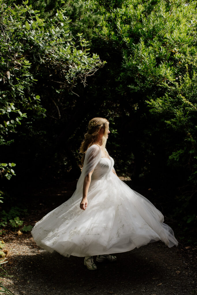 Bride with a full ball gown skirt embroidered with dinosaurs twirls in a pocket of forest light at Sue-Meg State Park in Northern California