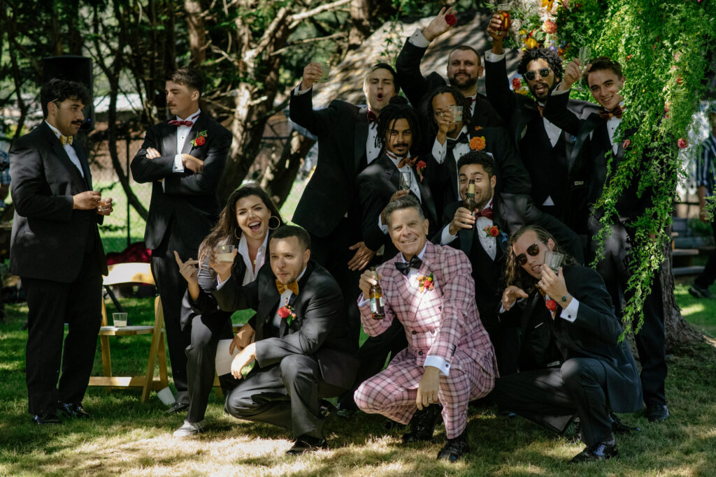 Grooms wedding crew poses under tree decorated in flowers at Fieldbrook wedding in Northern California