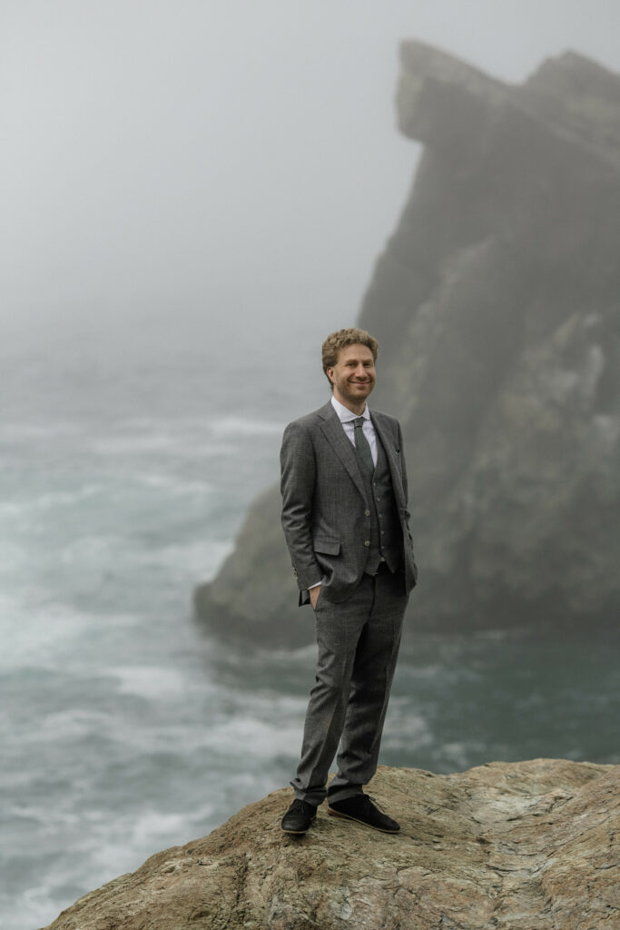 Portrait of groom in grey suit with green tie on rocky outcrop in Sue-Meg State Park during wedding portraits