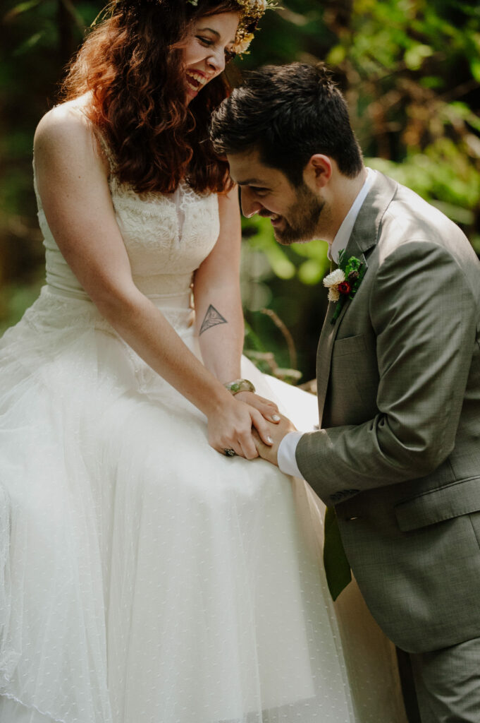 Couple laughs during first look in Northern California redwoods; bride wears vintage lace gown and straw flower crown