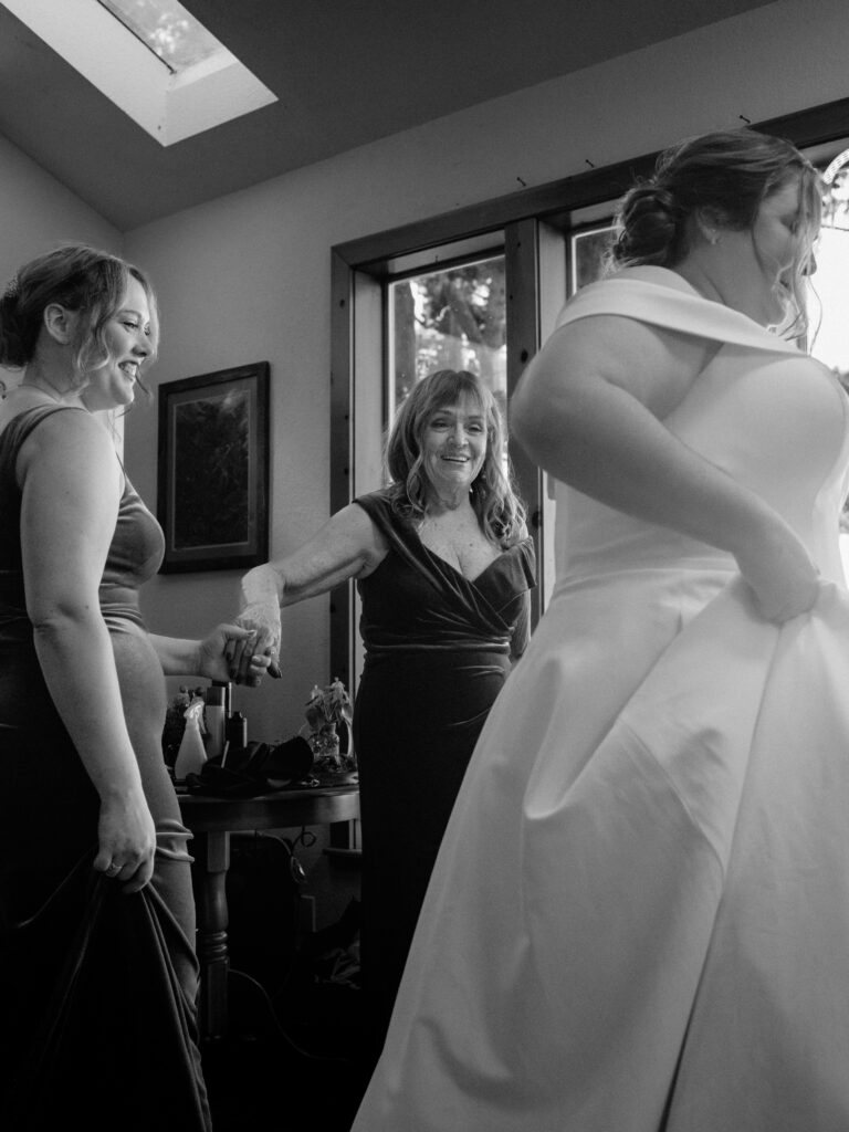 Mom grabs for hand of bridesmaid as she watches daughter get dressed before her wedding at the Lost Whale Inn