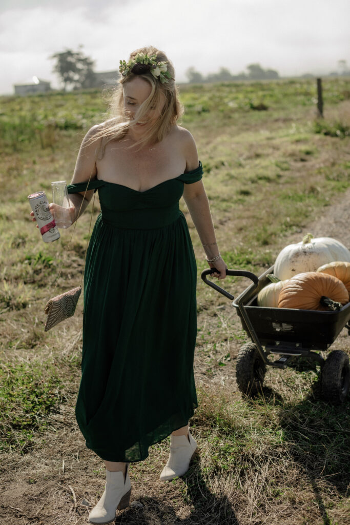 Wedding guest in strapless green midi dress pulls a wagon filled with pumpkins through a wedding reception in Northern California